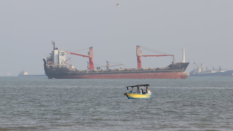 A boat floats as commercial vessels appear anchored in the Strait of Hormuz off Bandar Abbas,...
