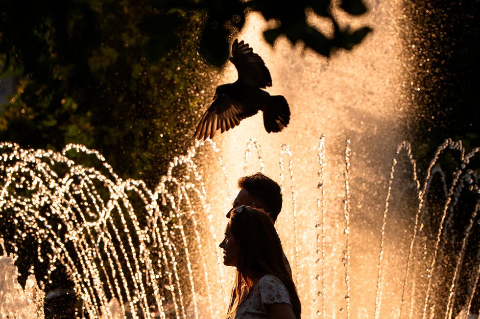 A couple walks by a public fountain on a torrid day, as the National Weather forecaster issued...